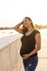 Portrait of a happy pregnant latina woman looking at side walking in a park at sunset. Pregnancy and motherhood concept.