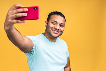 Positive young indian african american man smiling making selfie on smartphone camera, blogger communicating, recording video for followers in social networks. Isolated over yellow background.