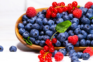 Blueberry, Red Currant and Raspberry With a Green Mint leaf in a Wooden Bowl on a white top view, Summer Freshly Berry, Copyspace