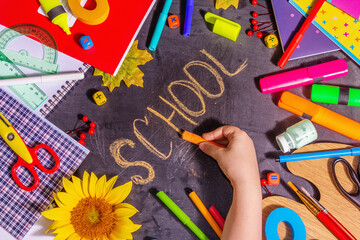 Children's hand writes the word "school" on a black chalkboard