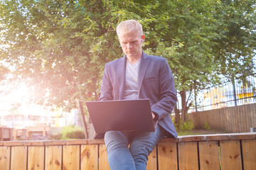 Fototapeta premium Young blond man in a jacket with a laptop and headphones. The concept of freelancing, remote study, work, business.