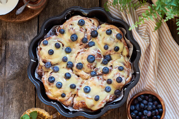Cinnamon rolls with white chocolate and blueberries. Brioche. Side view, wooden background, icing sugar, cocoa, yeast buns.
