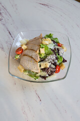 Glass bowl of chicken ceasar salad on a table