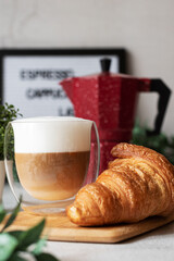 A cup of cappuccino with croissant on the table and a light background. Letterboard.