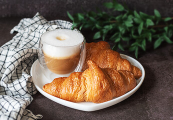 A cup of cappuccino with croissants on the table and a dark background.
