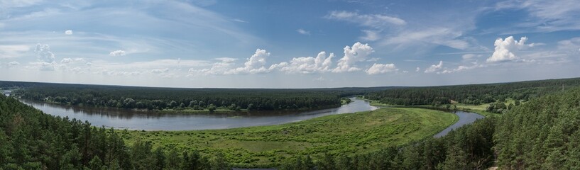 Panoramic view from the top of Merkine observation tower onto Nemunas river and surrounding riverbanks covered with green forest. Warm summer day. White clouds in blue sky.