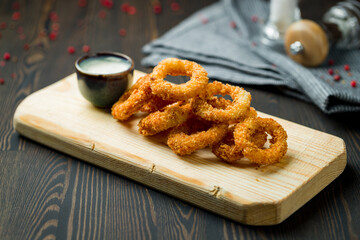 Rings of squid in batter with sauce on board on dark wooden table