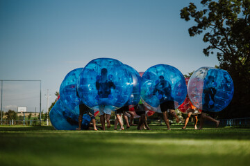 People playing in Bubble Football. Zorbing bumper football soccer on a green field