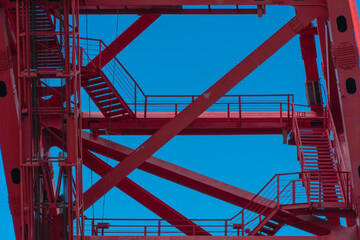 Red metal structures with stairs on a blue sky background, pattern or texture