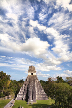 Vertical shot of Tikal under a blue cloudy sky in the daylight in Tikal, Guatemala