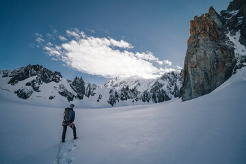 An alpinist on a glacier walking towards big alpine mountain. Climber on a alpine ascent in Mont Blanc massif near Chamonix, France. High alpine landscape and mountaineer on the climb towards summit.