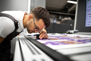 Worker checking print quality of graphics in modern printing house. - obrazy, fototapety, plakaty