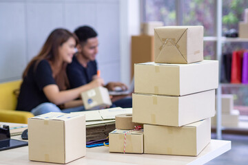 Close-up of parcel boxes on the table with a young couple working while sitting on a sofa in the office a blurred background. Concept of business and e-commerce