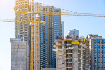 Fototapeta na wymiar Construction cranes and unfinished residential buildings against clear blue sky. Housing construction, apartment block with scaffolding
