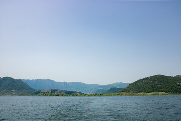 Landscape with lake and green mountains against the background of a clear sky. Panoramic beautiful view on largest lake. Wonderful summer day.