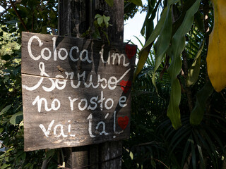 placa de madeira em meio a vegetação tropical com a mensagem pitada em branco de motivação e coragem para encarar o dia a dia.