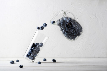 Blueberry levitation. Blueberries from a jug are poured into a glass beaker on a white background. Making a berry smoothie. Abstract creative concept.