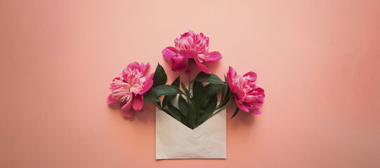 White envelope with pink peonies inside on a pink background