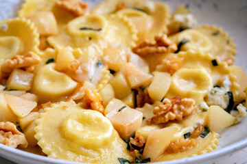 Cooked ravioli with pumpkin, pear, nuts and honey in a white plate on table. Italian dish pasta ravioli, close-up