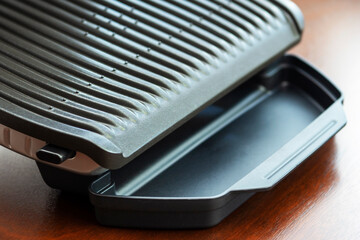  A gadget for preparation of healthy food. electric grill on kitchen table for indoor barbecue. Ridge surface of an electric grill