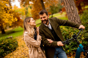 Fototapeta premium Young couple in the autumn park with electrical bicycle