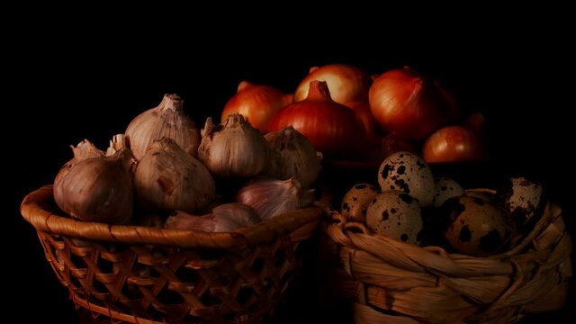 Quail eggs, bulbs of garlic and onion in wicker baskets on black background. Concept of agriculture, organic products and eco-friendly lifestyle
