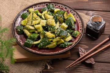 Broken cucumbers in a plate sprinkled with sesame seeds, on a wooden background.
