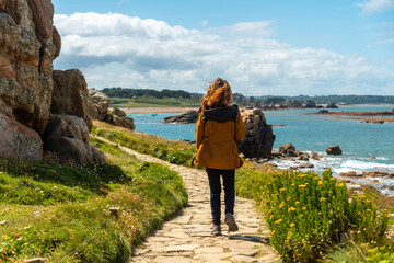 A young woman walking along the paths of the beautiful coastline at low tide of Le Gouffre de Plougrescant, Cote de Granit Rose, Cotes d'Armor, Brittany, France - obrazy, fototapety, plakaty