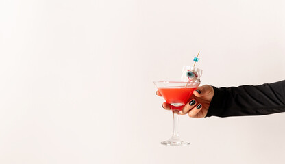 Woman hand with black nails holding glass with scary red halloween cocktail on white background