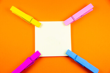 Blank yellow sticker with colorful wooden clothespins. Close up of note paper on orange background. Copy space.