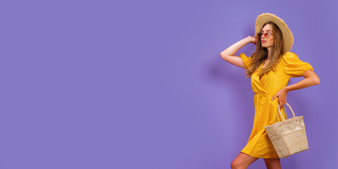 Beautiful young woman in white dress, summer straw hat, sunglasses, straw bag isolated on pastel violet background. 