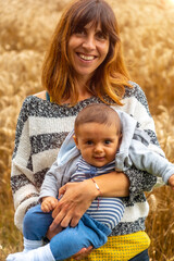 Fototapeta na wymiar A young smiling mother with her baby in a yellow straw field in French Brittany in the summer of July, near the Broceliande forest. France