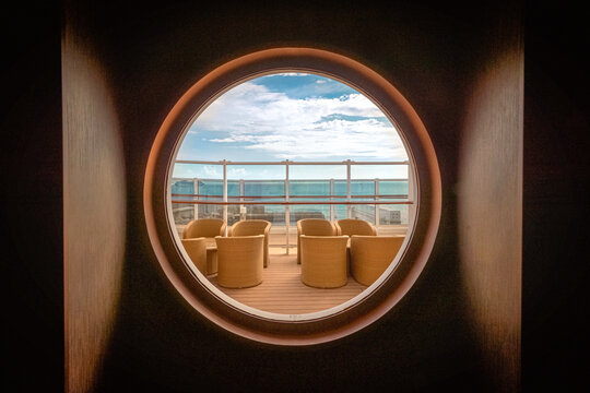 Vue d'un salon ext&eacute;rieur sur le pont promenade d'un navire de croisi&egrave;re &agrave; travers un hublot.	
