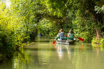 Fototapeta na wymiar A young couple rowing the boat sailing between La Garette and Coulon, Marais Poitevin the Green Venice, near the town of Niort, France