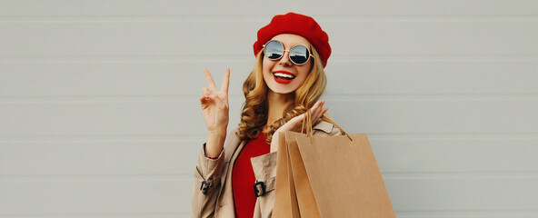 Autumn portrait of cheerful happy smiling woman with shopping bags wearing a red french beret on gray background