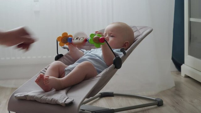 Cute 3 month old baby boy playing with toys in bouncer for kids, infant activity, child playing with wooden toys in rocking chair. High quality 4k footage