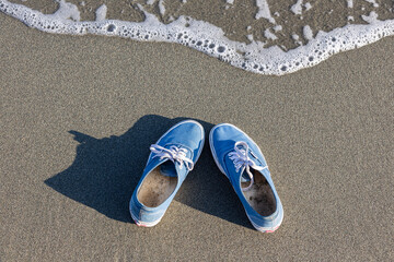 blue sneakers casting a shadow lie on the beach with a looming wave