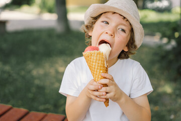 Boy in a hat is holding an ice cream and looks happy and surprised. Summer food and summer time
