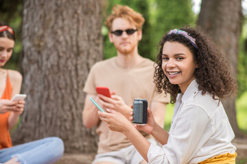 Mulatta girl with drink and smartphone and friends behind