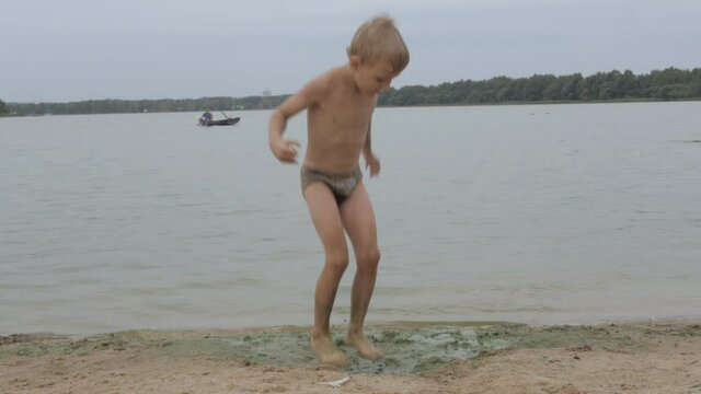 Little barefoot boy jumping in muddy puddle at the beach