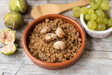 Close-up of a typical Spanish dish called Migas, accompanied by grapes and figs, on a rustic wooden background.