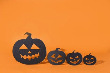 Four paper pumpkins with carved faces casting shadow on orange background, halloween symbols.