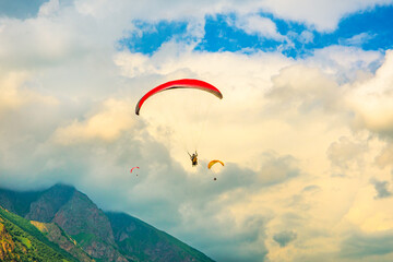 Fototapeta na wymiar A paraglider flies high in the mountains against the background of an epic sky