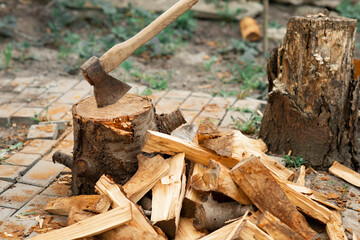 Ax and firewood in the yard. Ax in the stump. Pile of firewood and tree stump. Firewood for the winter.