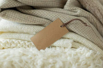Pile of knitted clothes and empty label. Place for your text. Warm background, knitwear, space for text. Sale of clothes