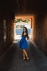 Portrait happy young woman wearing blue dress laughing looking at camera standing on street. Urban background