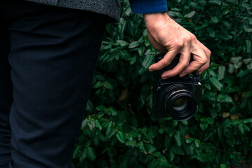 Male hand holding a vintage film camera in the air. Green nature in the background.