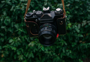 Male hand holding a vintage film camera in the air. Green nature in the background.