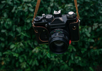 Male hand holding a vintage film camera in the air. Green nature in the background.