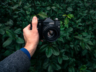Male hand holding a vintage film camera in the air. Green nature in the background.